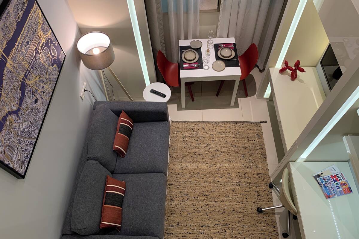 Una sala de estar moderna con un sofá gris, una mesita redonda y una zona de comedor con una mesa blanca y sillas rojas.