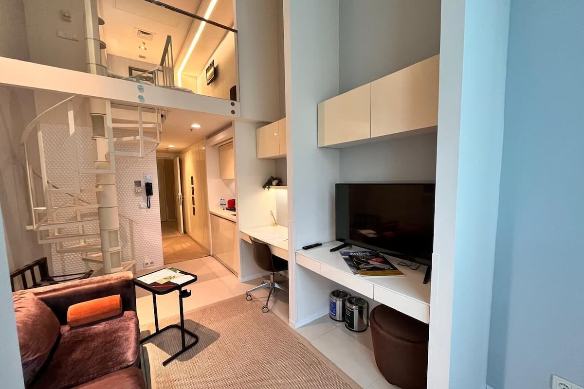 Un apartamento moderno con un entrepiso con habitación, una sala de estar con televisor y una kitchenette.