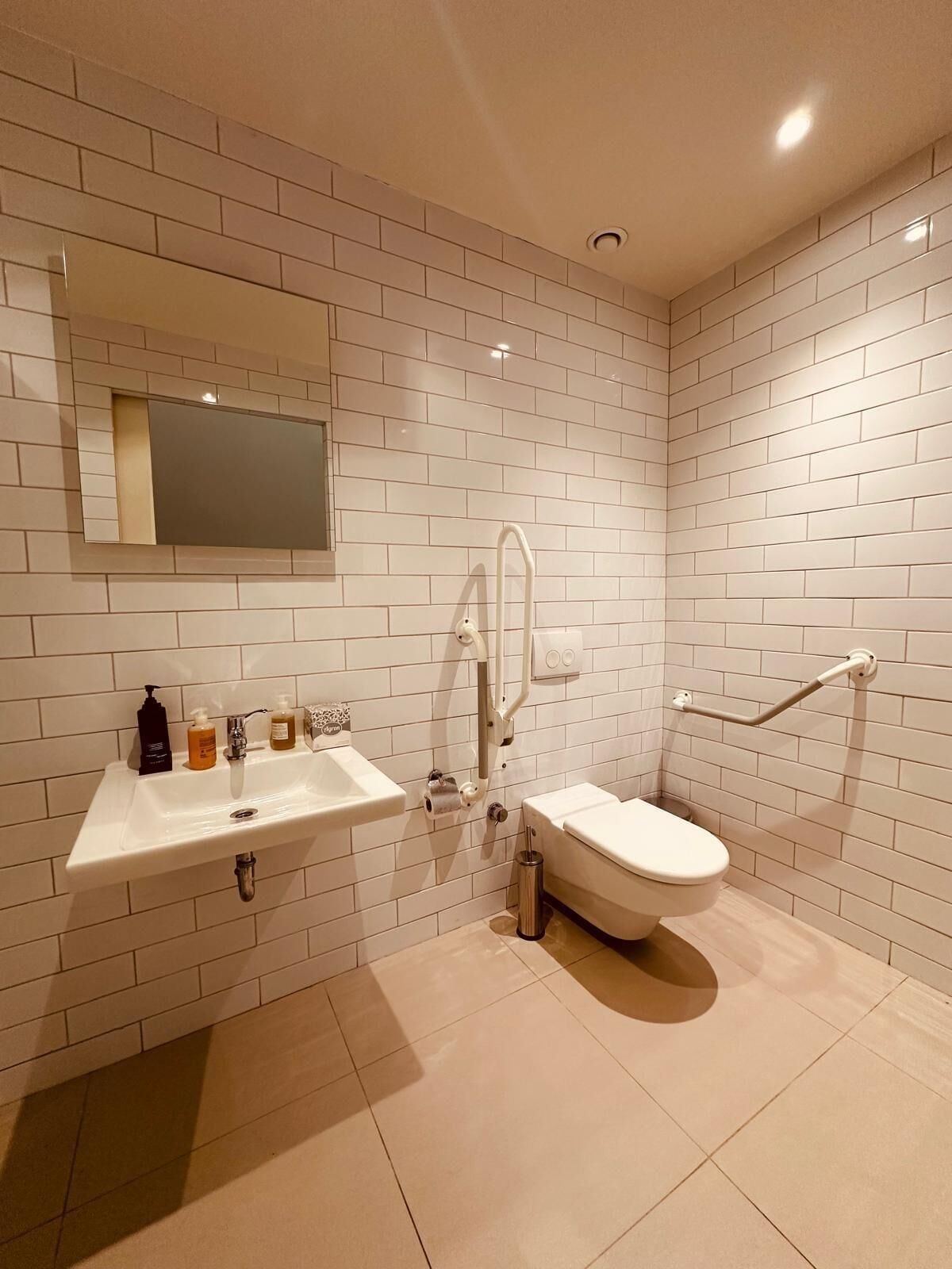 A modern bathroom with white subway tiles, a sink, a toilet, and a mirror.