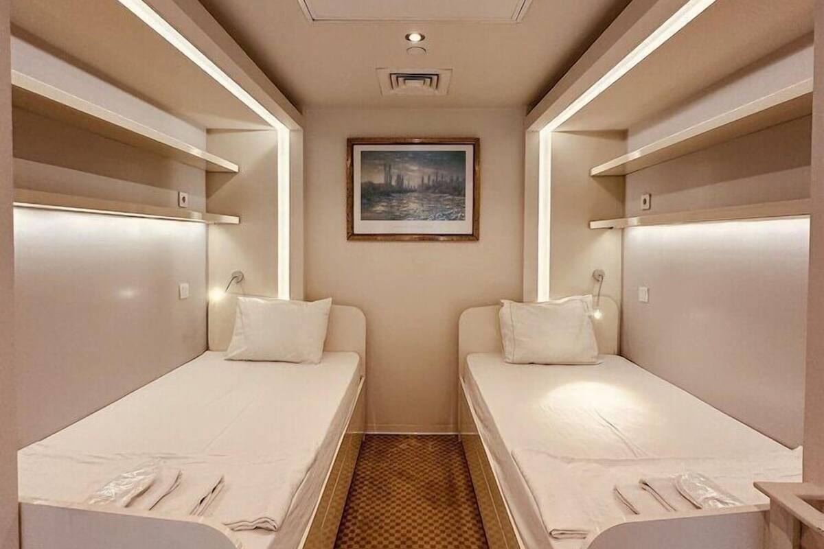 Habitación de hotel estrecha con dos camas, alfombra a cuadros y un cuadro en la pared.