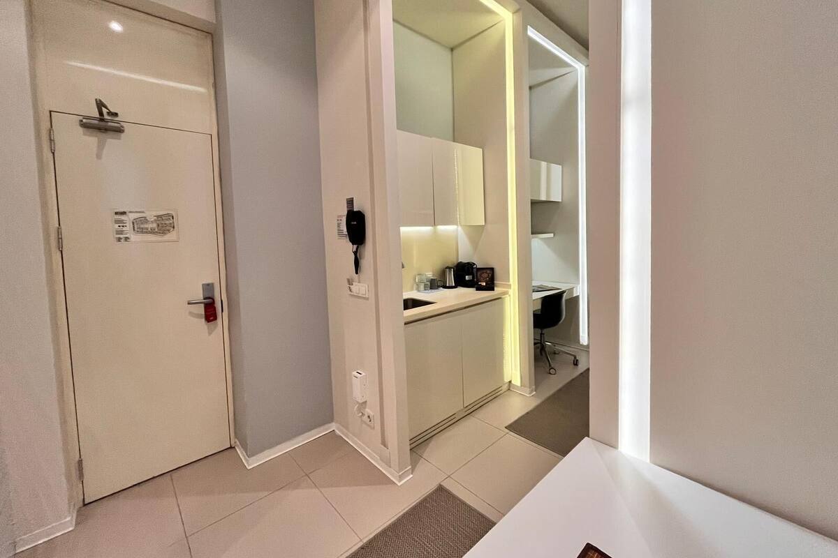 Una habitación de hotel moderna con puerta, espejo y una pequeña zona de kitchenette.