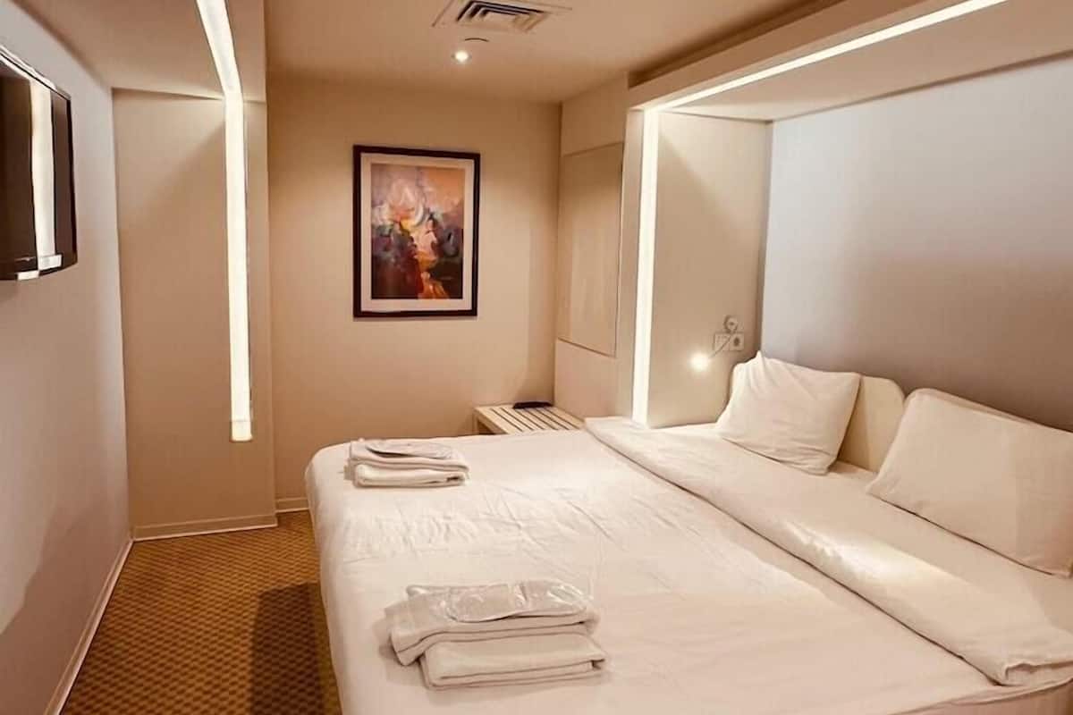 Una habitación de hotel moderna con una cama grande, un televisor de pantalla plana, un cuadro en la pared y una alfombra estampada.