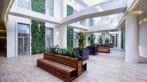 A spacious atrium with a wooden bench, planters with greenery, and a high ceiling with natural light. - Ortaköy Aparts (Istanbul)