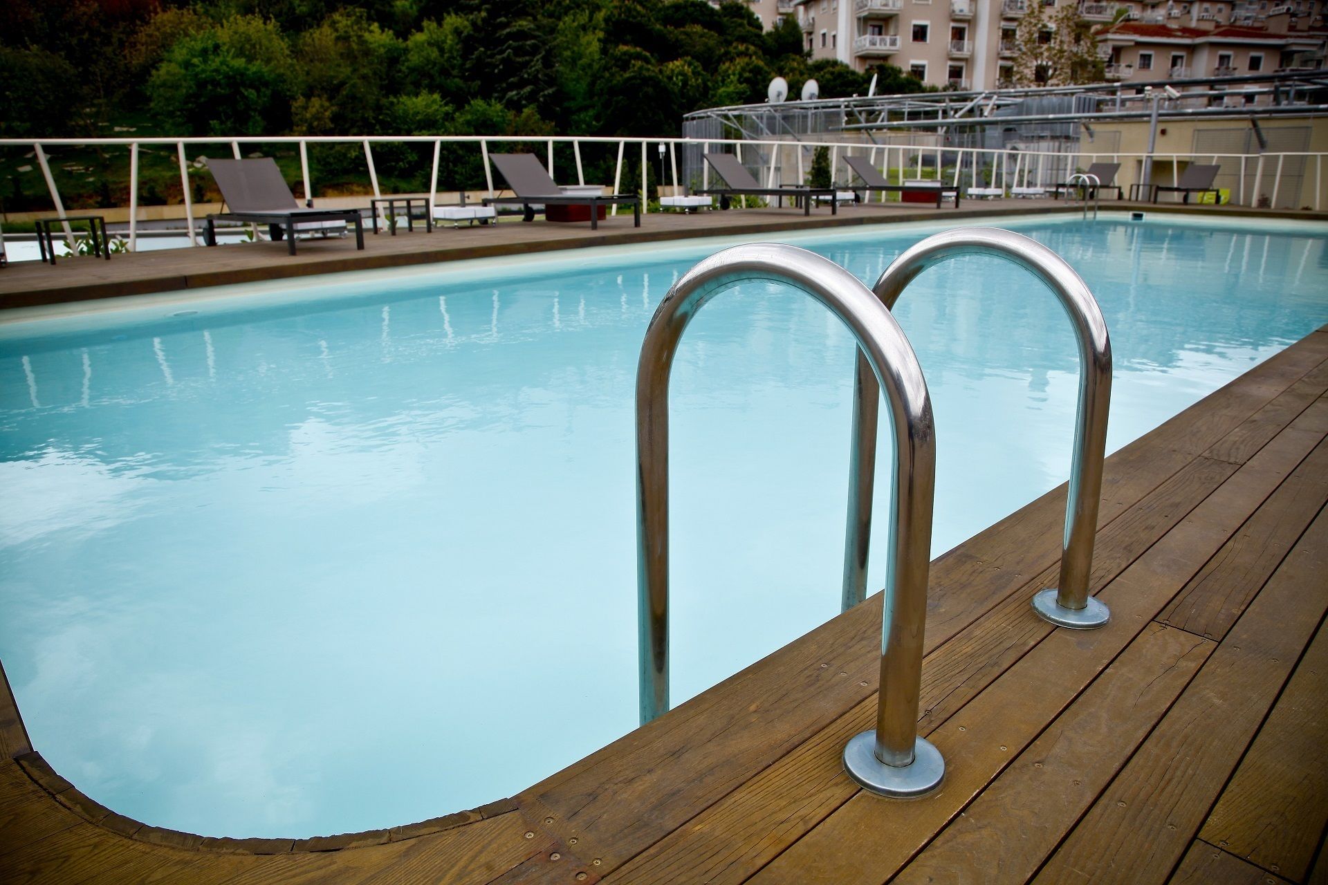Una piscina con barandillas metálicas en una terraza de madera, rodeada de sillas de descanso y un edificio al fondo.