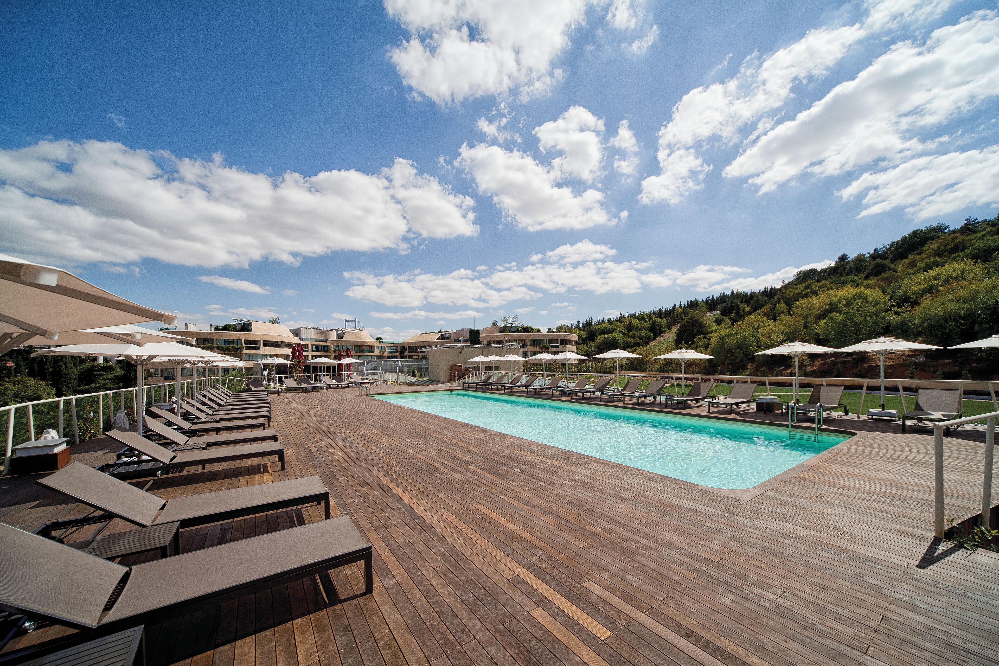 A wooden deck with a pool, lounge chairs, and umbrellas.