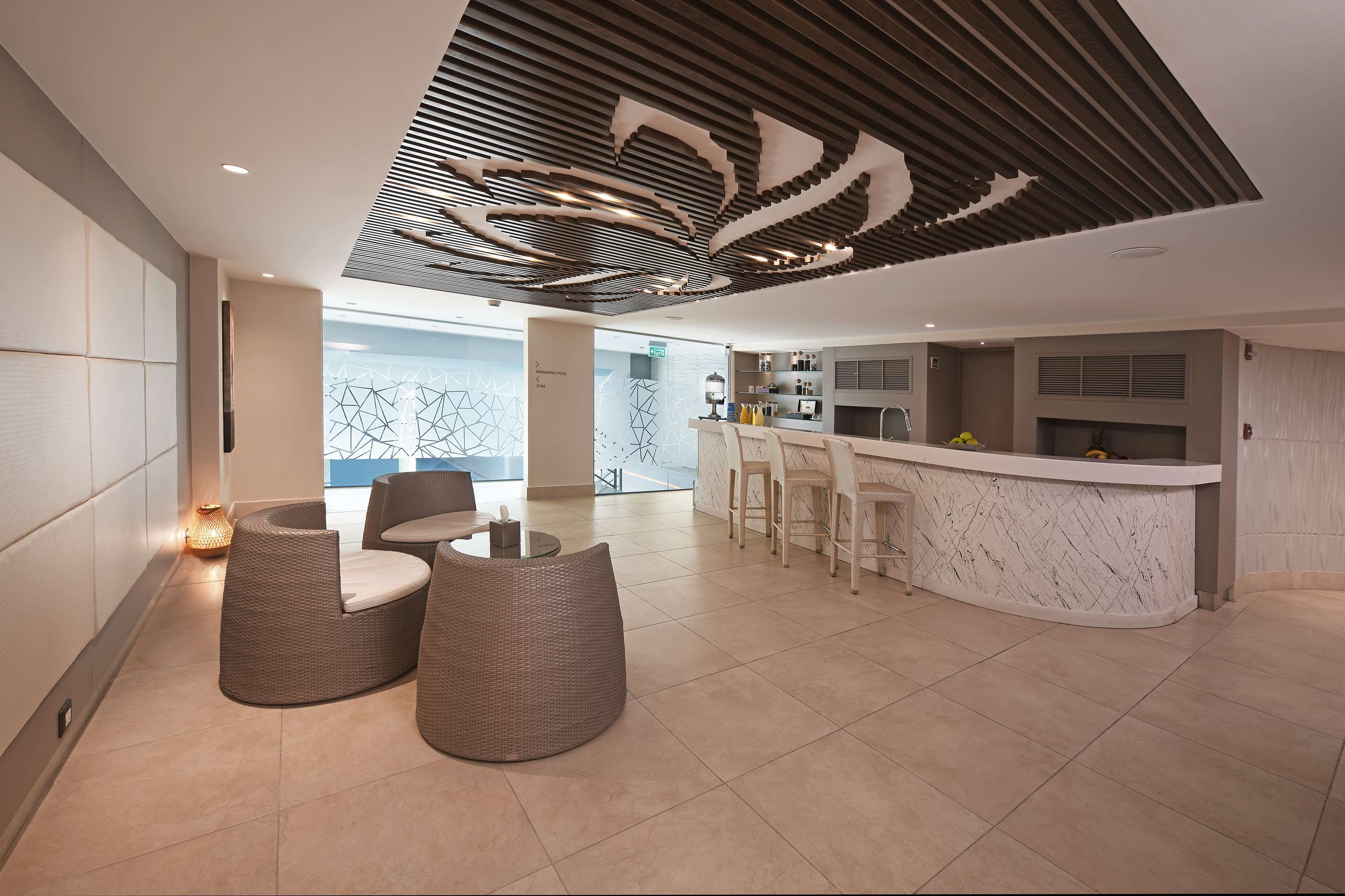 A modern interior with a curved bar, wicker seating, and a geometric ceiling design.