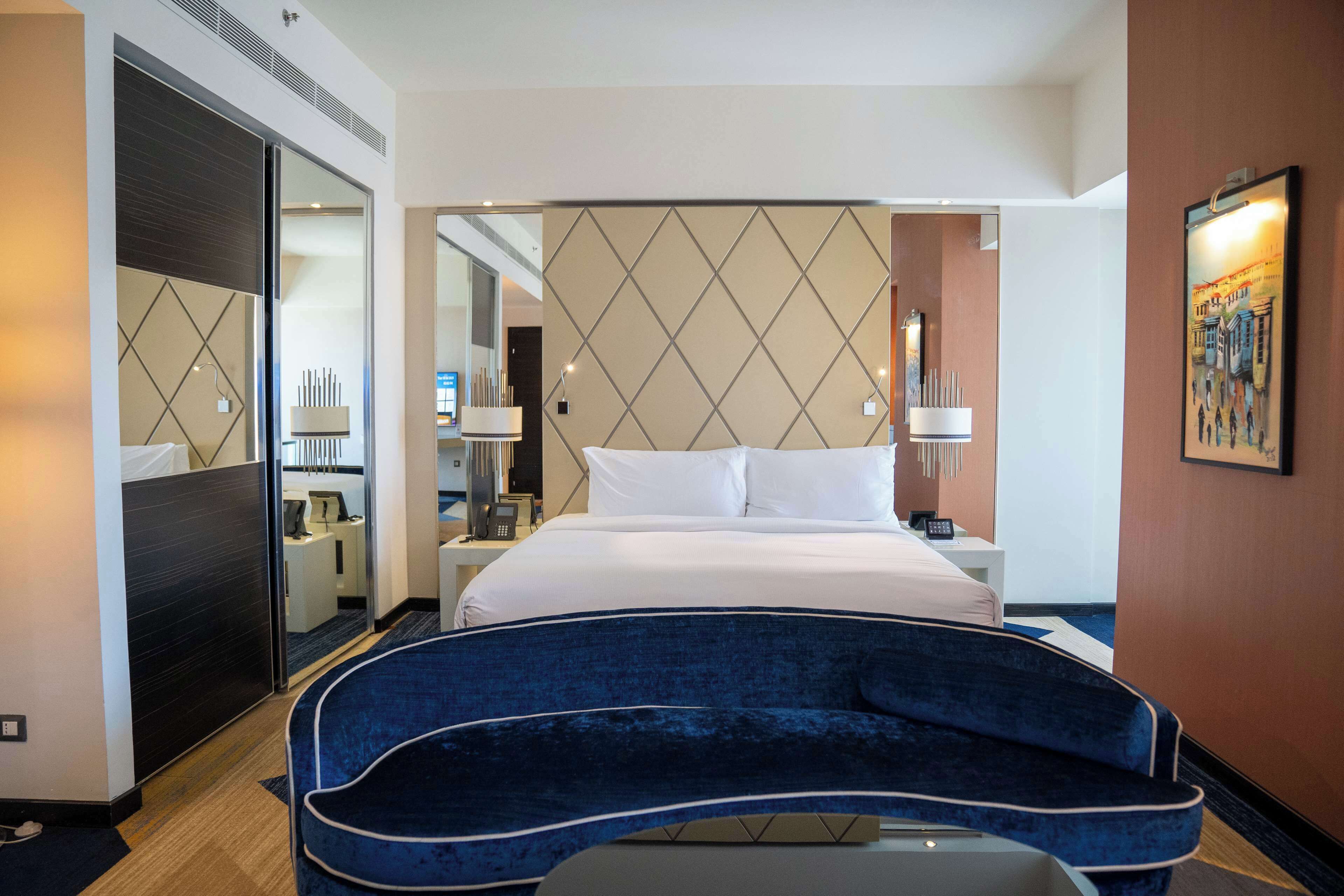 Une chambre d’hôtel avec un lit, un bureau, une chaise, un miroir et un tableau au mur.