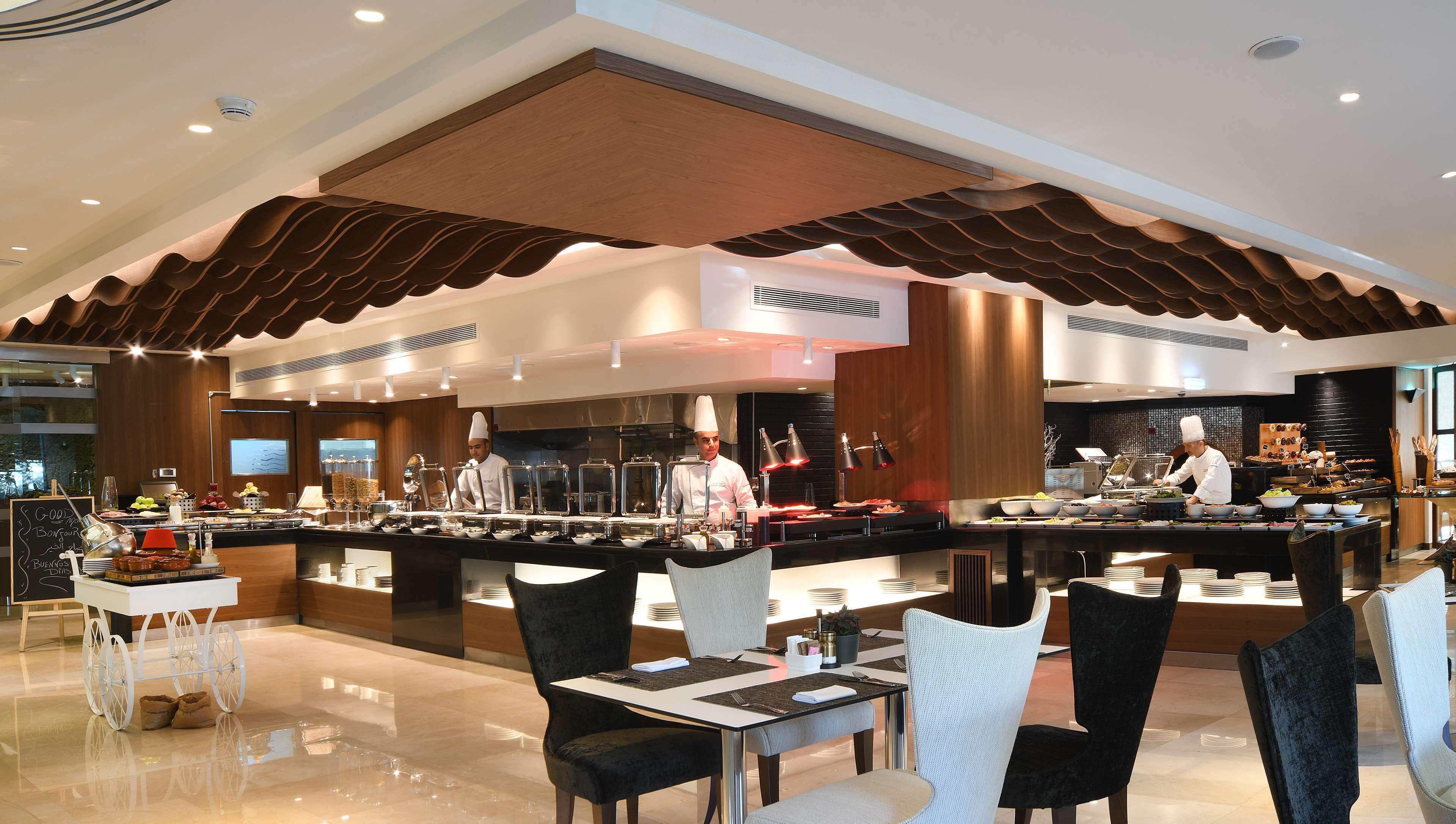 A modern restaurant with a buffet setup, chefs at work, and a clean, contemporary interior.