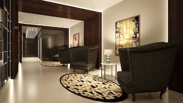 A modern hotel lobby with a geometric patterned rug, dark upholstered chairs, a small side table with a lamp, and a large abstract painting on the wall.