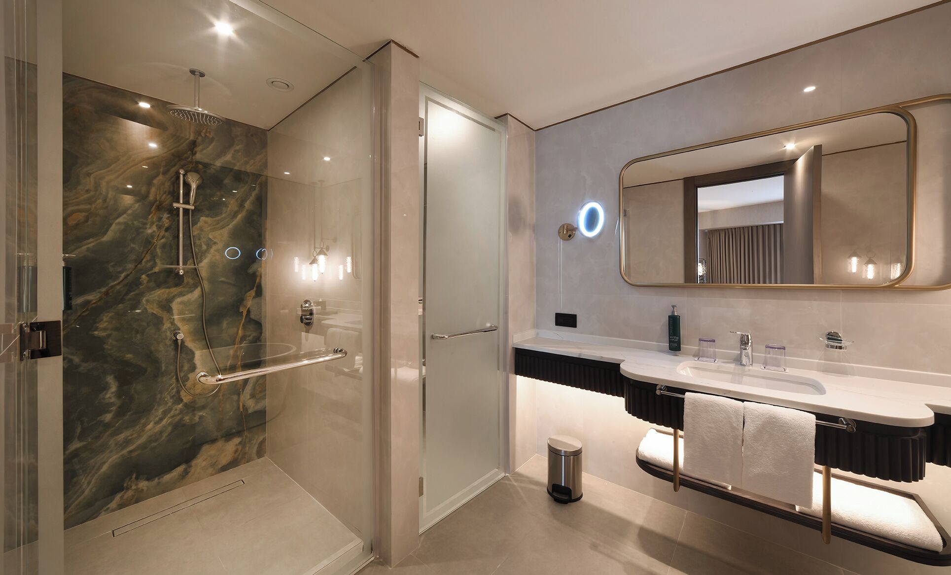 A modern bathroom with a glass-enclosed shower, a large mirror, and a vanity with a towel rack.