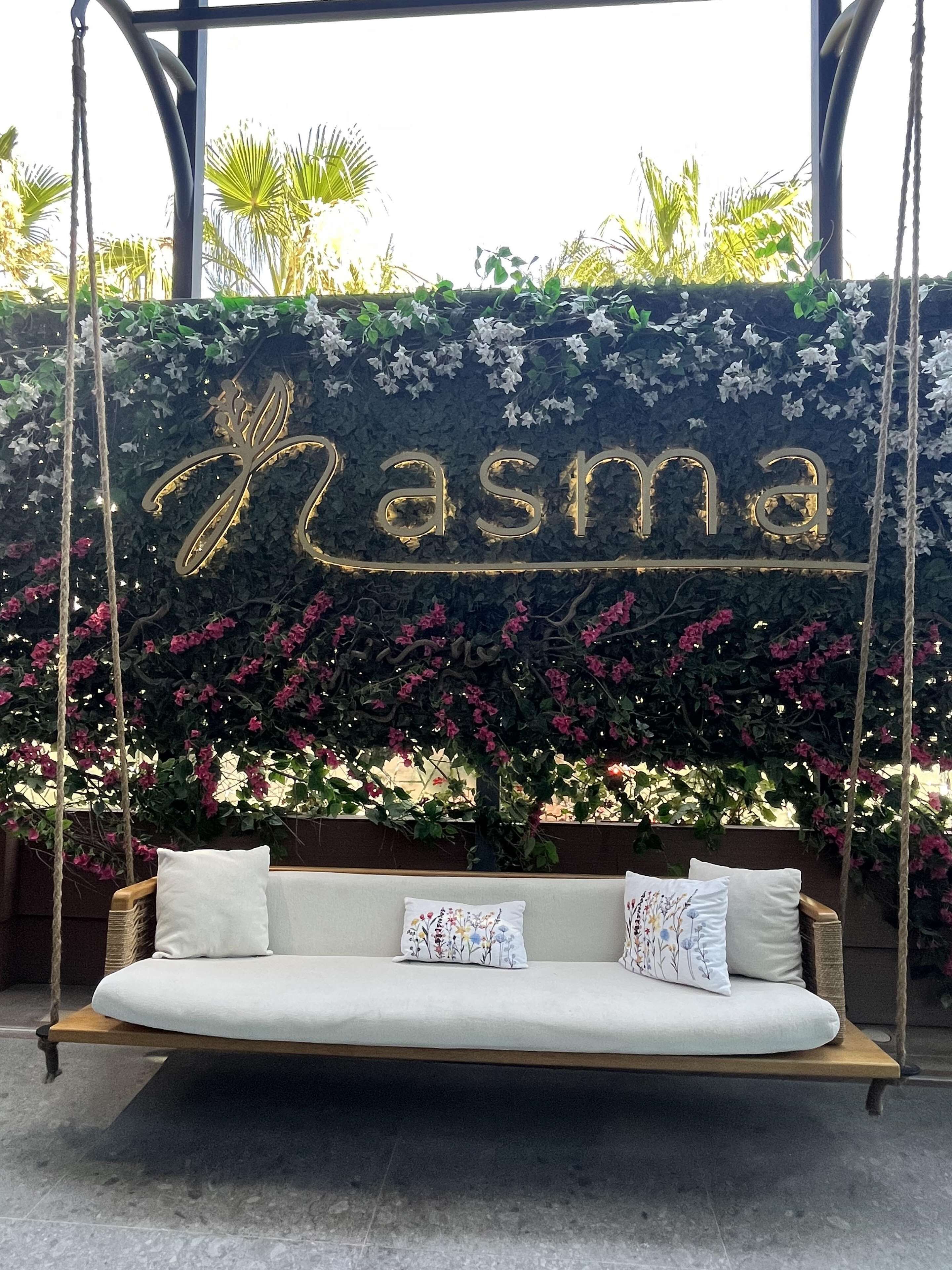 Un fauteuil suspendu avec un coussin et un mur décoratif sur lequel on peut voir le mot « Masma » en arrière-plan.