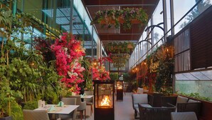 Un espace de restauration intérieur avec des tables et des chaises, un foyer central et des plantes suspendues.
