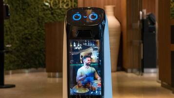 A robot with a screen displaying a chef, in a modern lobby with a green wall and a large vase.