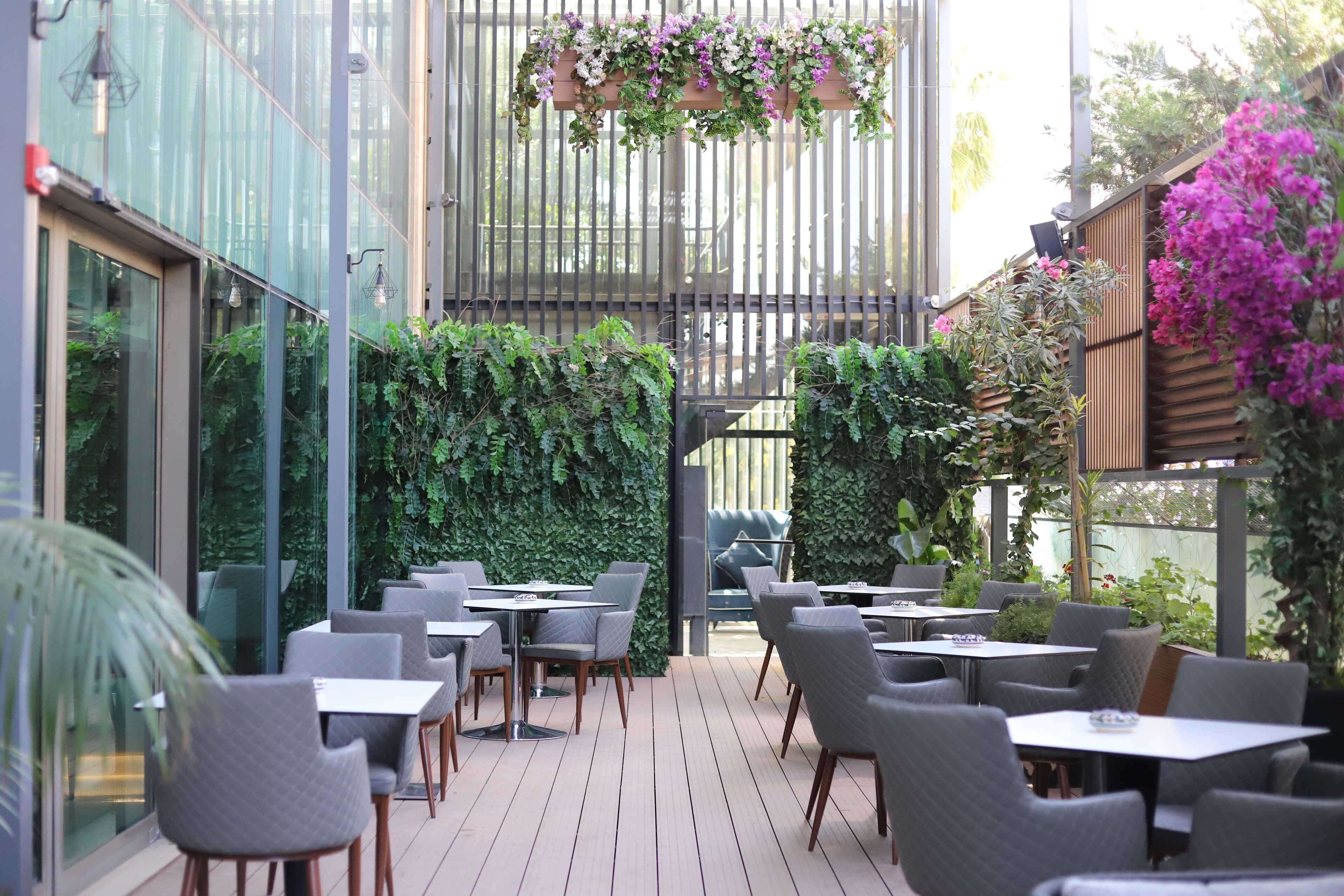 An outdoor patio area with tables and chairs, surrounded by lush greenery and a wooden fence.