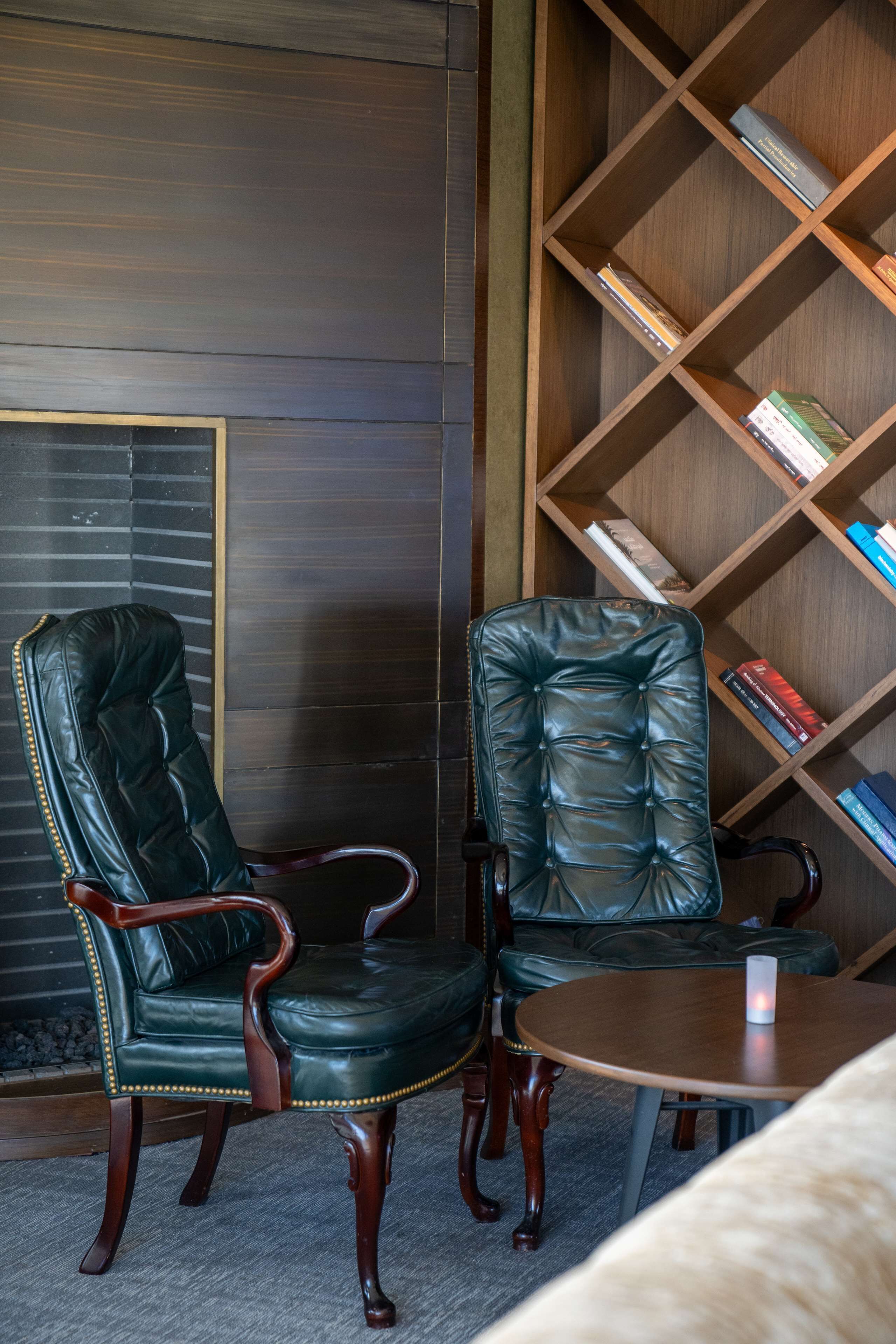 A room with two leather chairs, a wooden bookshelf, and a small round table.