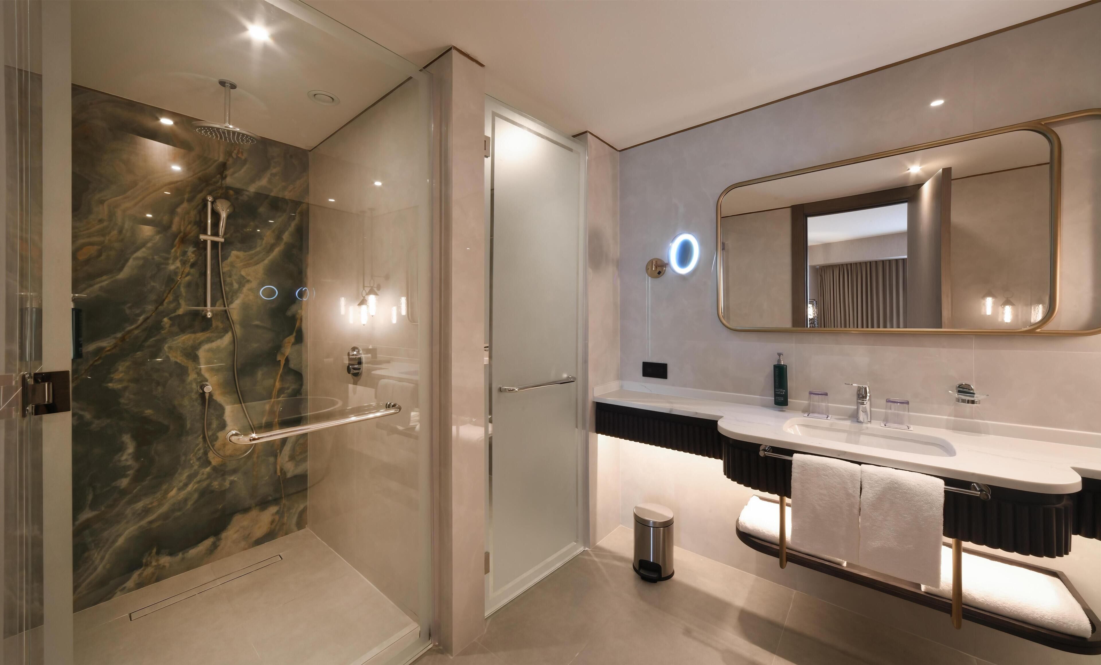 A modern bathroom with a glass-enclosed shower, a vanity with a large mirror, and a towel rack.