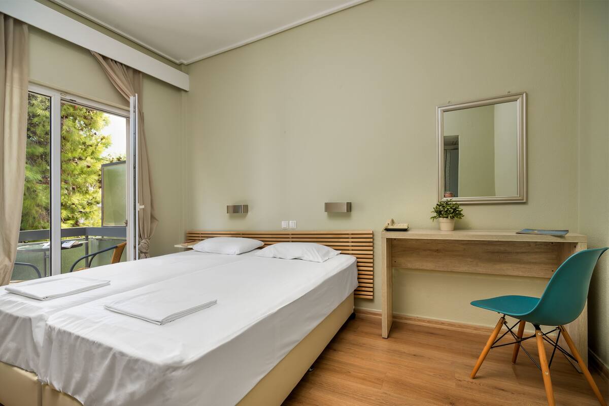 A hotel room with a bed, a desk, a chair, a mirror, and a window with curtains.