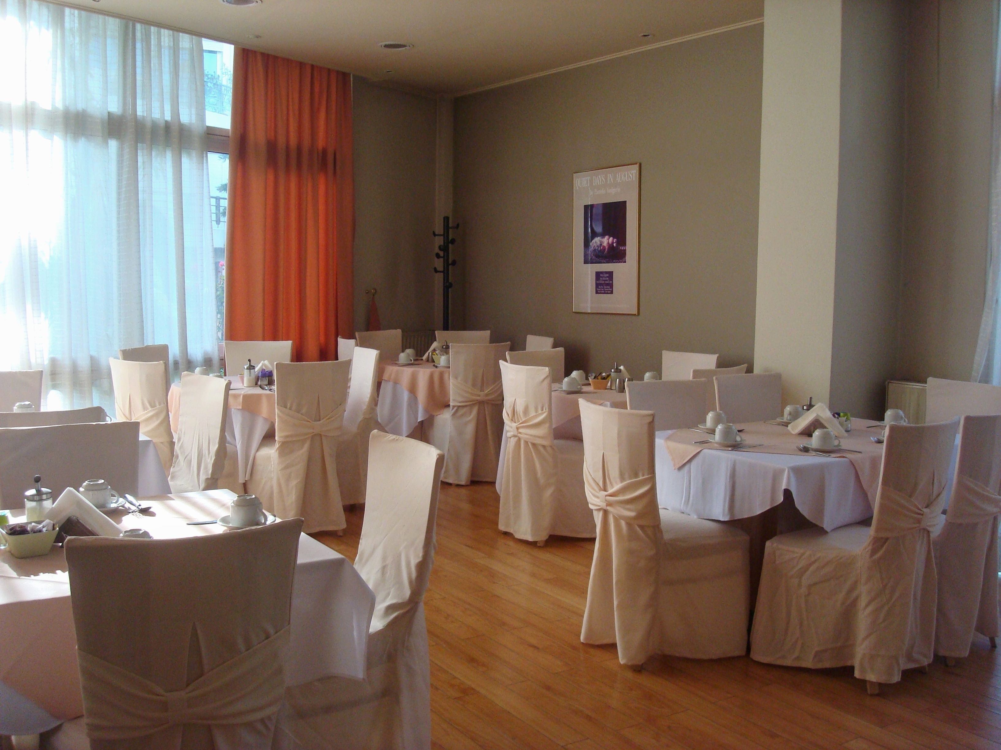 A dining area with tables set for a formal event, featuring white tablecloths and chairs with white coverings.