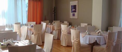 A dining area with tables set for a formal event, featuring white tablecloths and chairs with white coverings.
