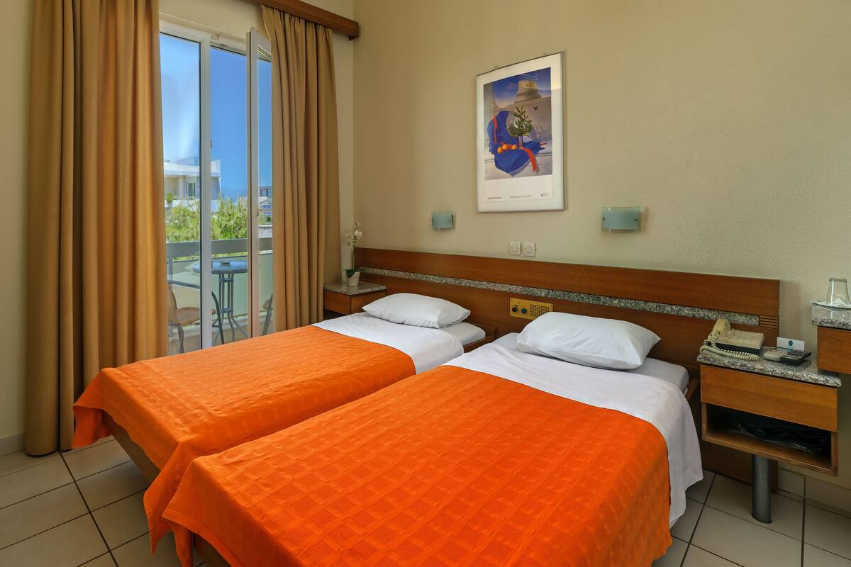 A hotel room with two beds, a balcony, a framed picture on the wall, and a bedside table with a phone and a lamp.