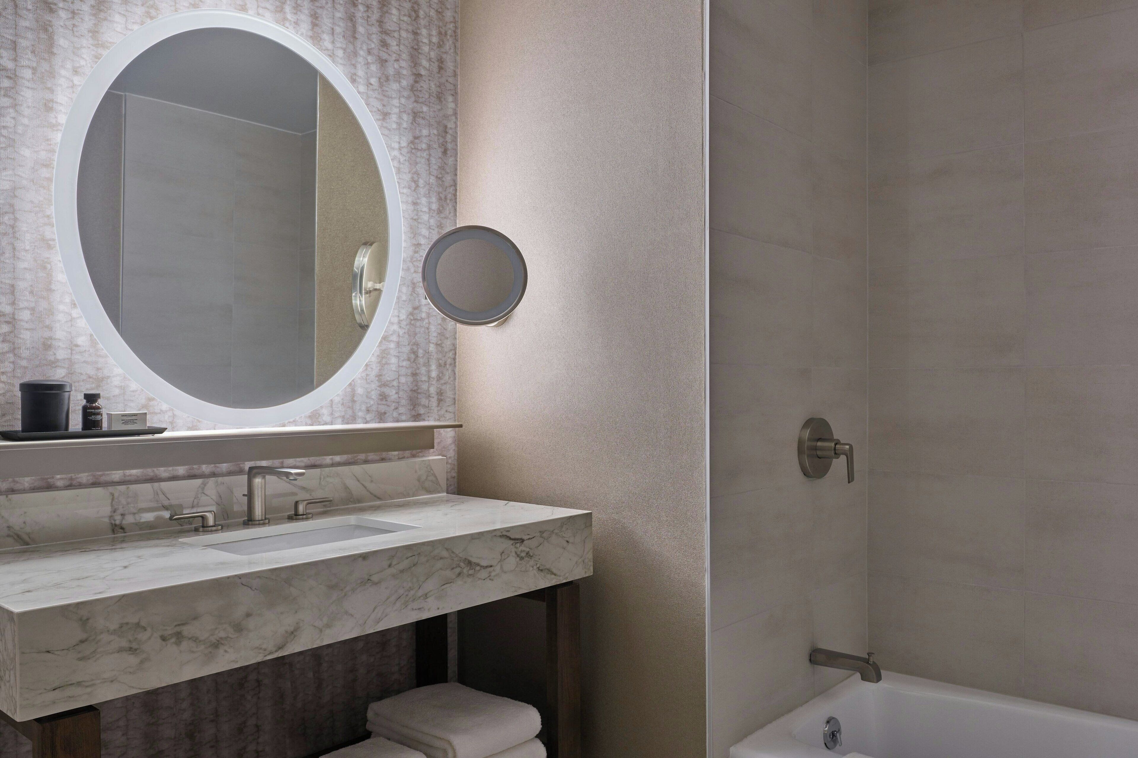 Une salle de bain avec un lavabo en marbre, un miroir rond, une baignoire et un porte-serviettes.