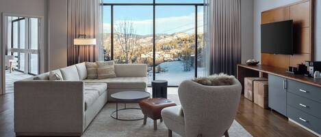 A modern living room with a sofa, armchair, coffee table, and a TV mounted on the wall.