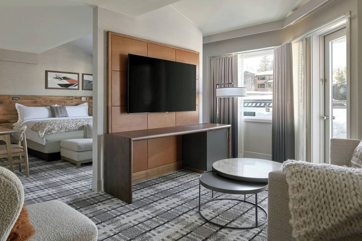 Une chambre d’hôtel avec un lit, un téléviseur fixé au mur, une petite table et une vue sur l’extérieur par une fenêtre.