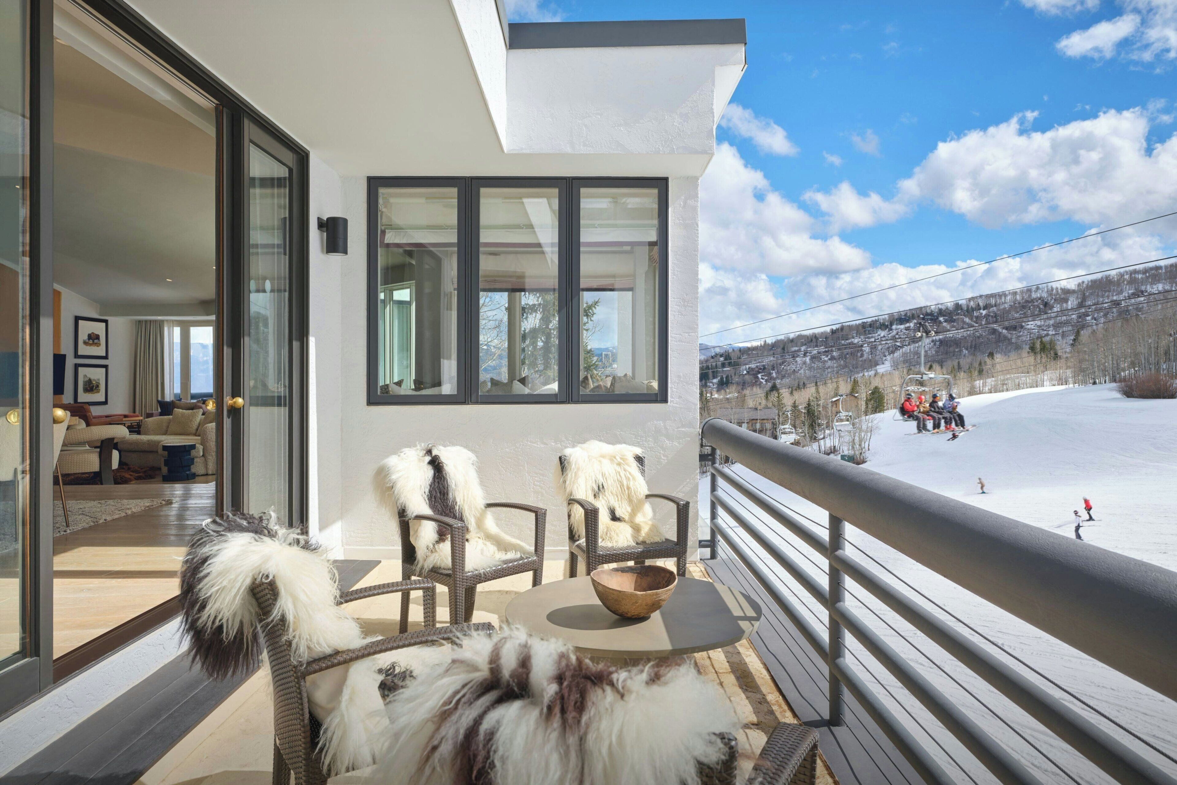 A balcony with wicker chairs and a bowl, overlooking a snowy landscape with a ski lift in the distance.