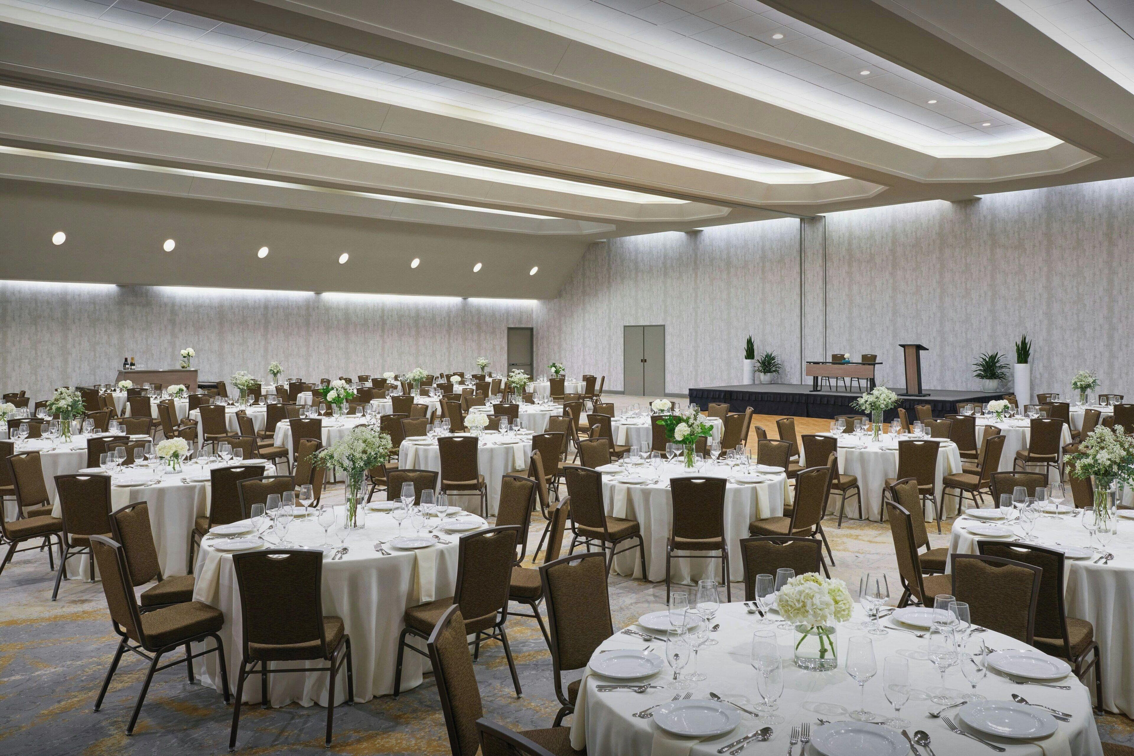 A large banquet hall with round tables set for dining, arranged in rows.