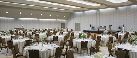 A large banquet hall with round tables set for dining, arranged in rows.