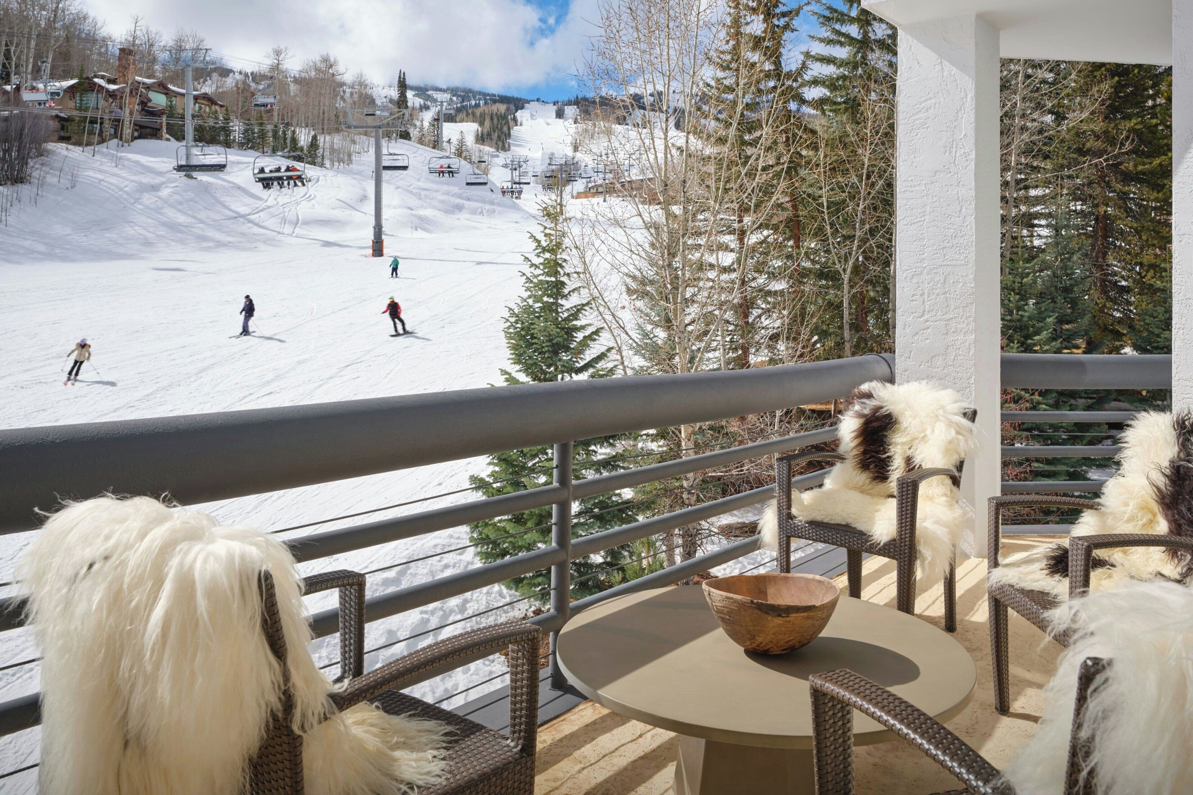 A balcony with wicker furniture, a round table, and a view of a ski slope with skiers.