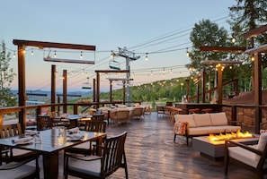 An outdoor patio with wooden tables and chairs, a sofa, and a fire feature. - Viewline Resort Snowmass, Autograph Collection (Snowmass Village)