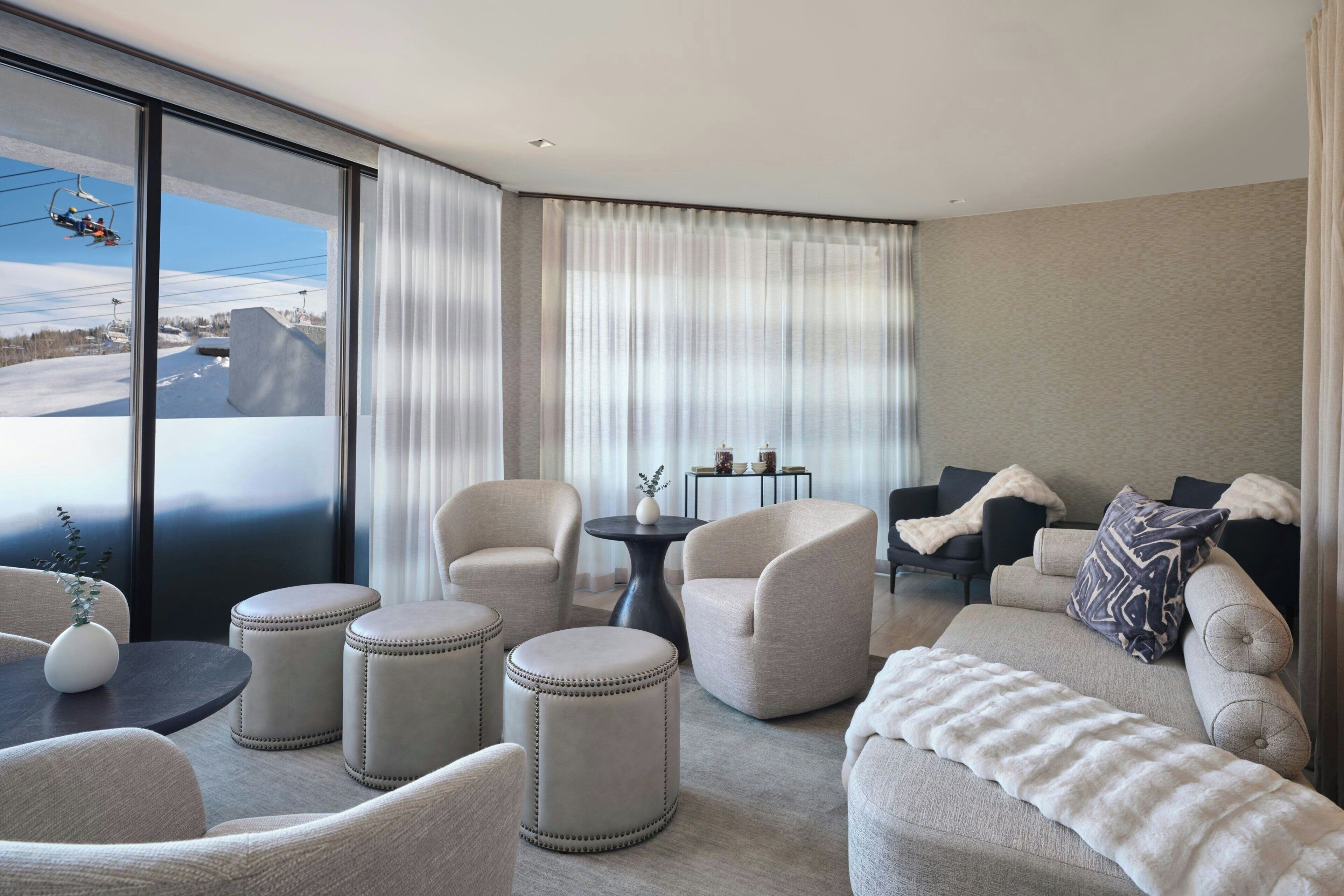 Una sala de estar moderna con sofá, sillones, otomanas, una mesa de centro y vistas de un telesilla.