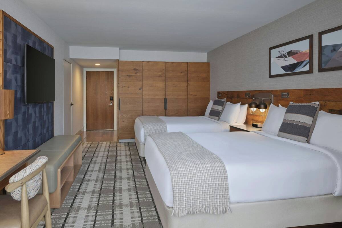 Une chambre d’hôtel avec un lit, des tables de chevet, un téléviseur, une armoire en bois et des œuvres d’art accrochées au mur.