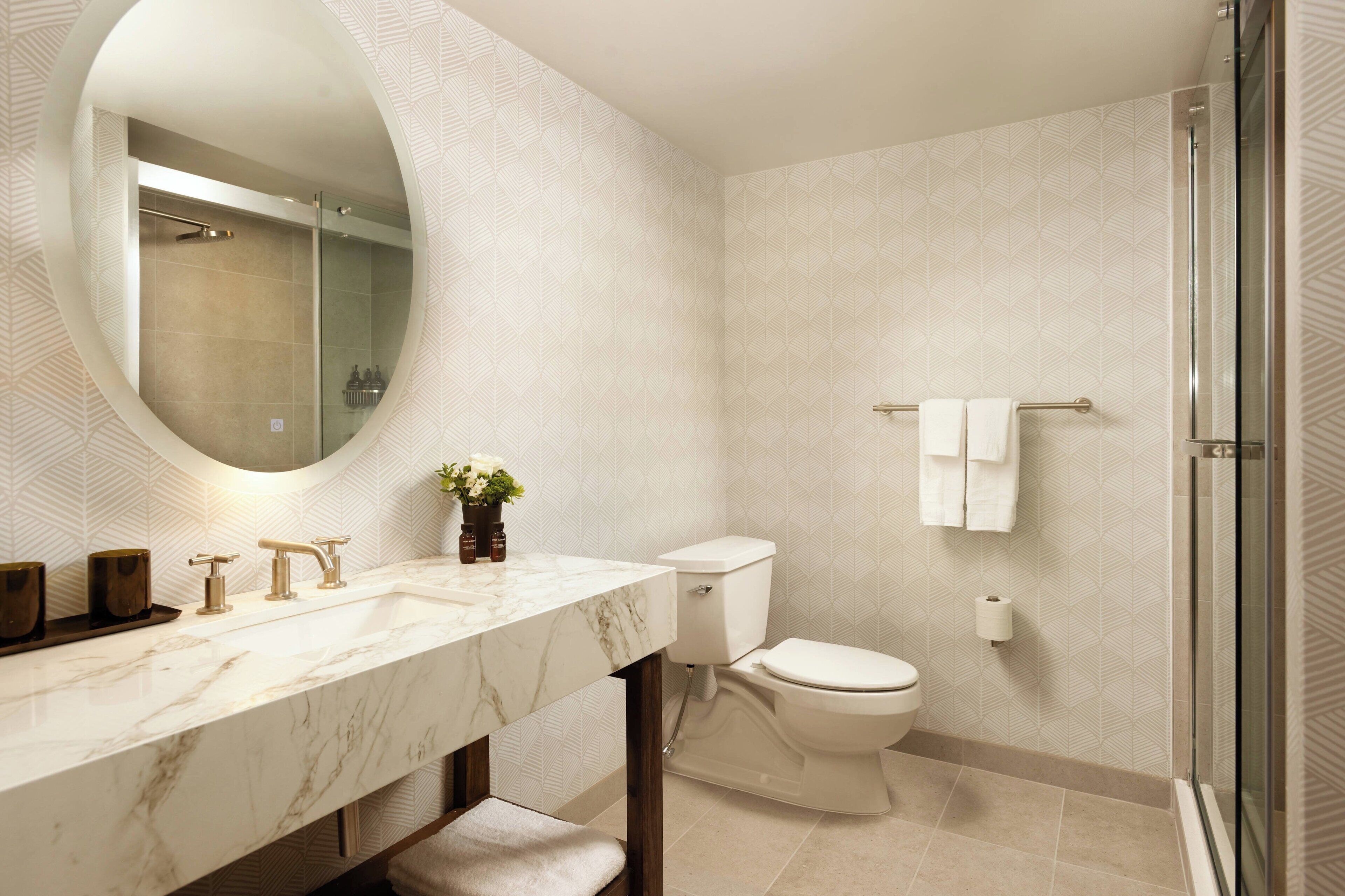A modern bathroom with a marble vanity, a toilet, and a glass shower enclosure.