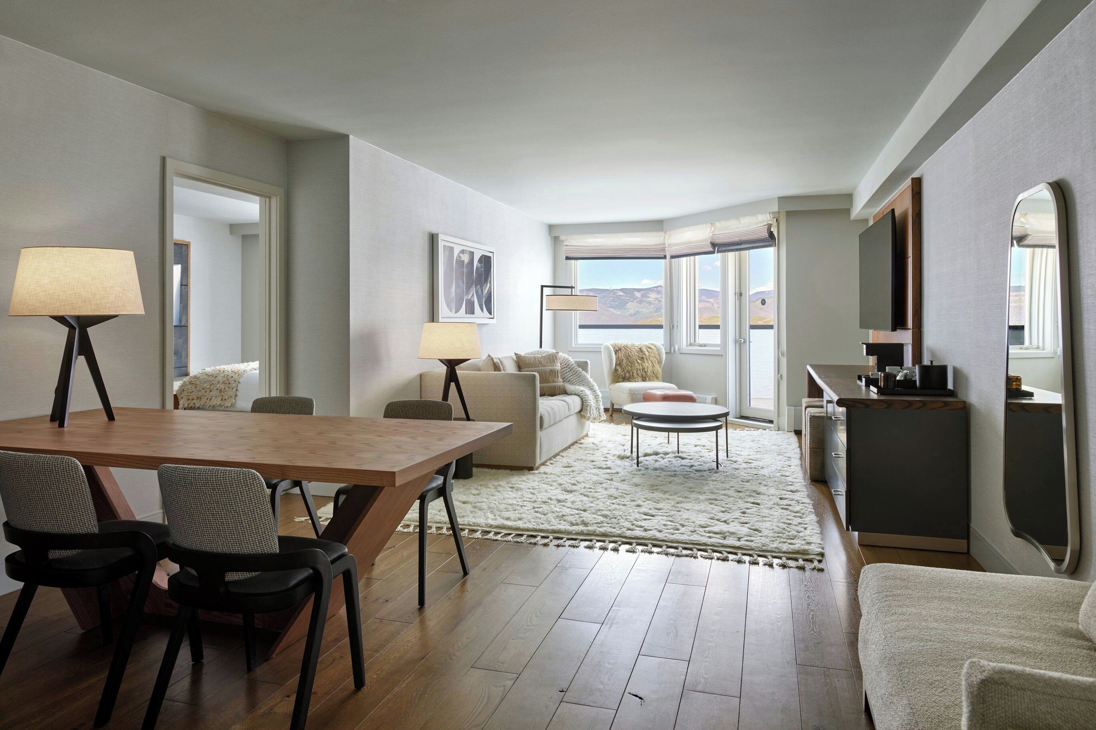 A modern living room with a wooden dining table, two chairs, a sofa, a coffee table, and a TV.