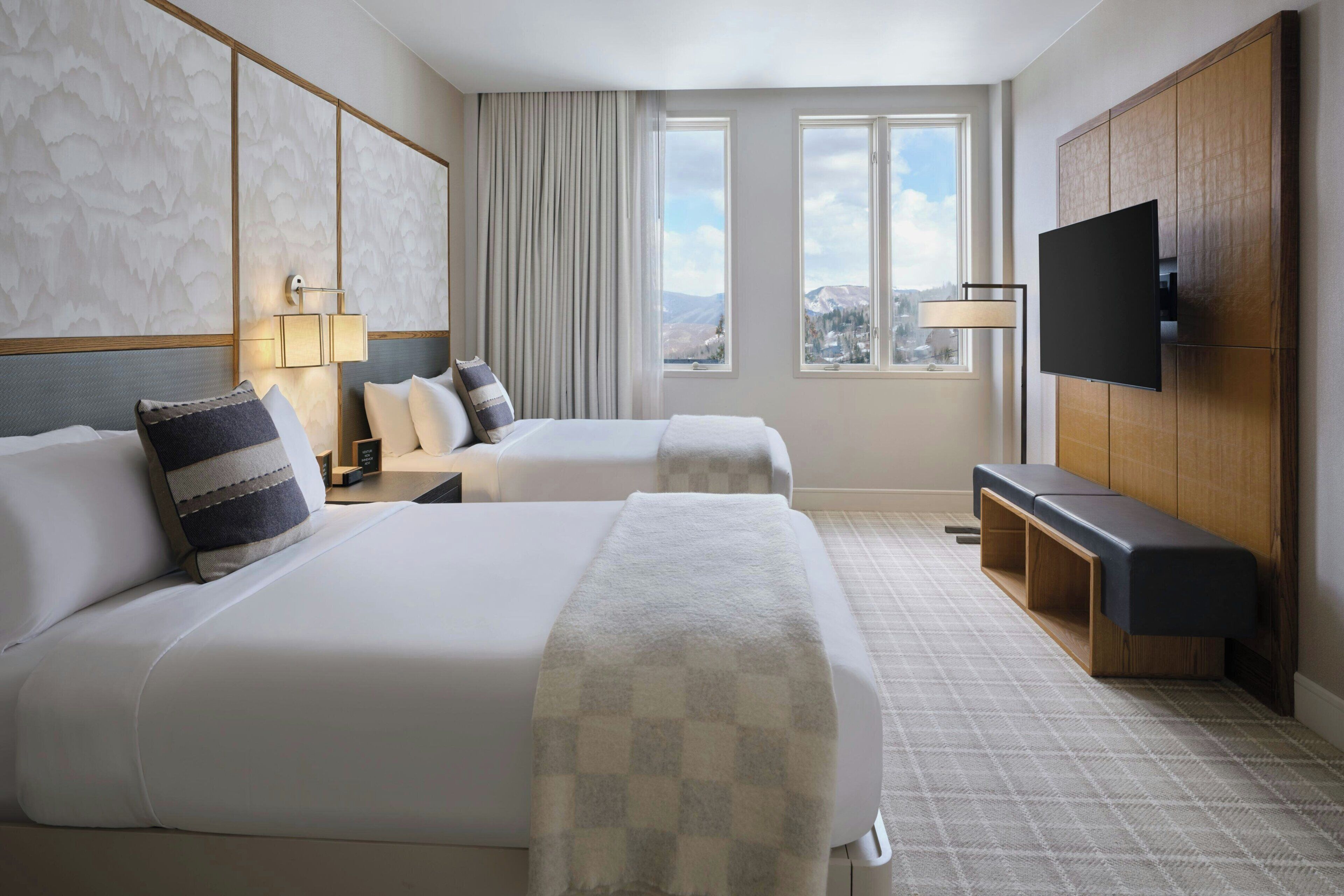 Habitación de hotel con dos camas, televisión, escritorio y vistas a las montañas.