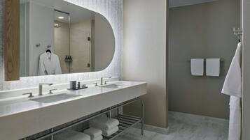 A modern bathroom with a large mirror, two sinks, a towel rack, and a shower area.