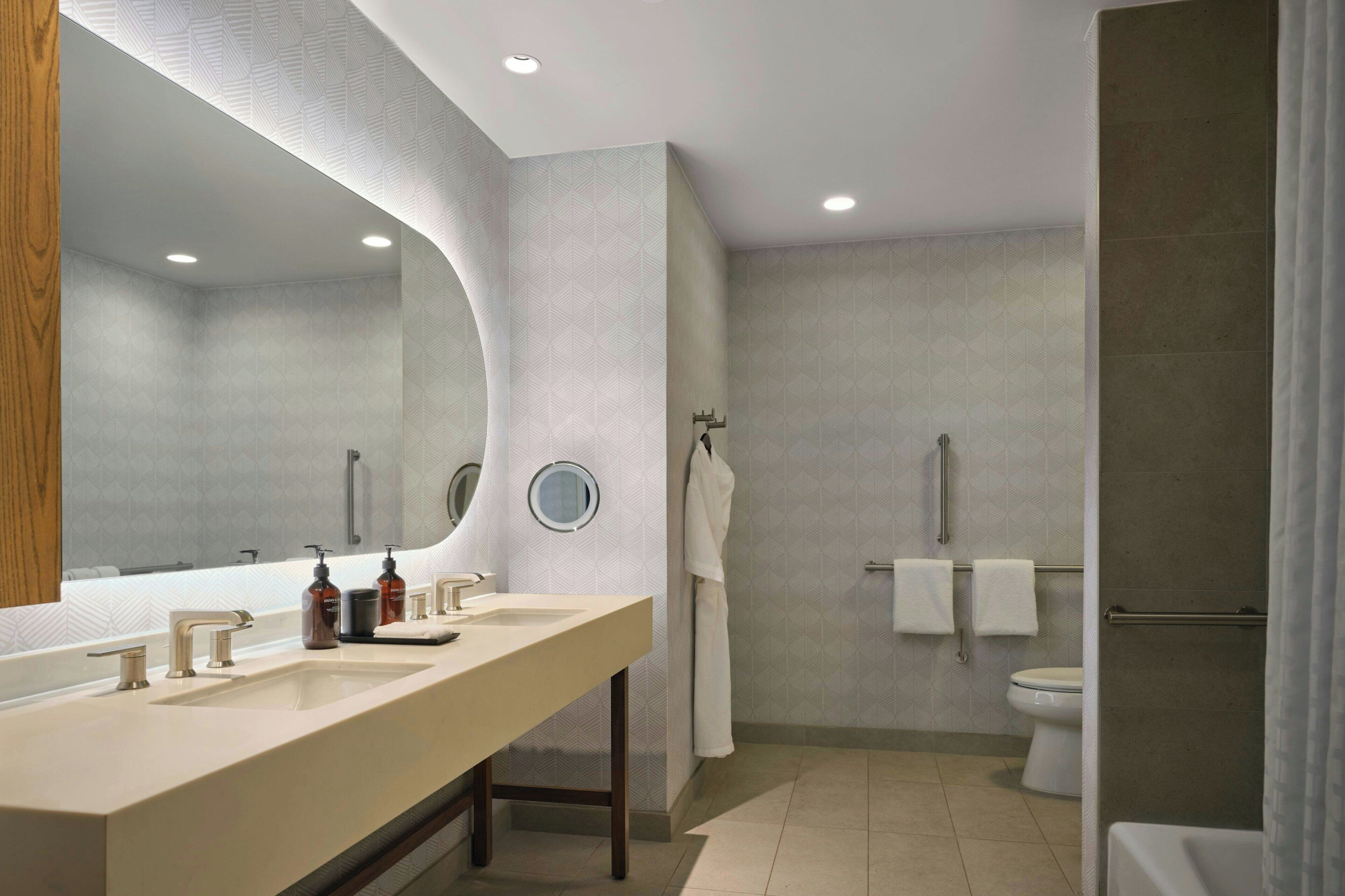 A modern bathroom with a large mirror, two sinks, a toilet, and a shower area.
