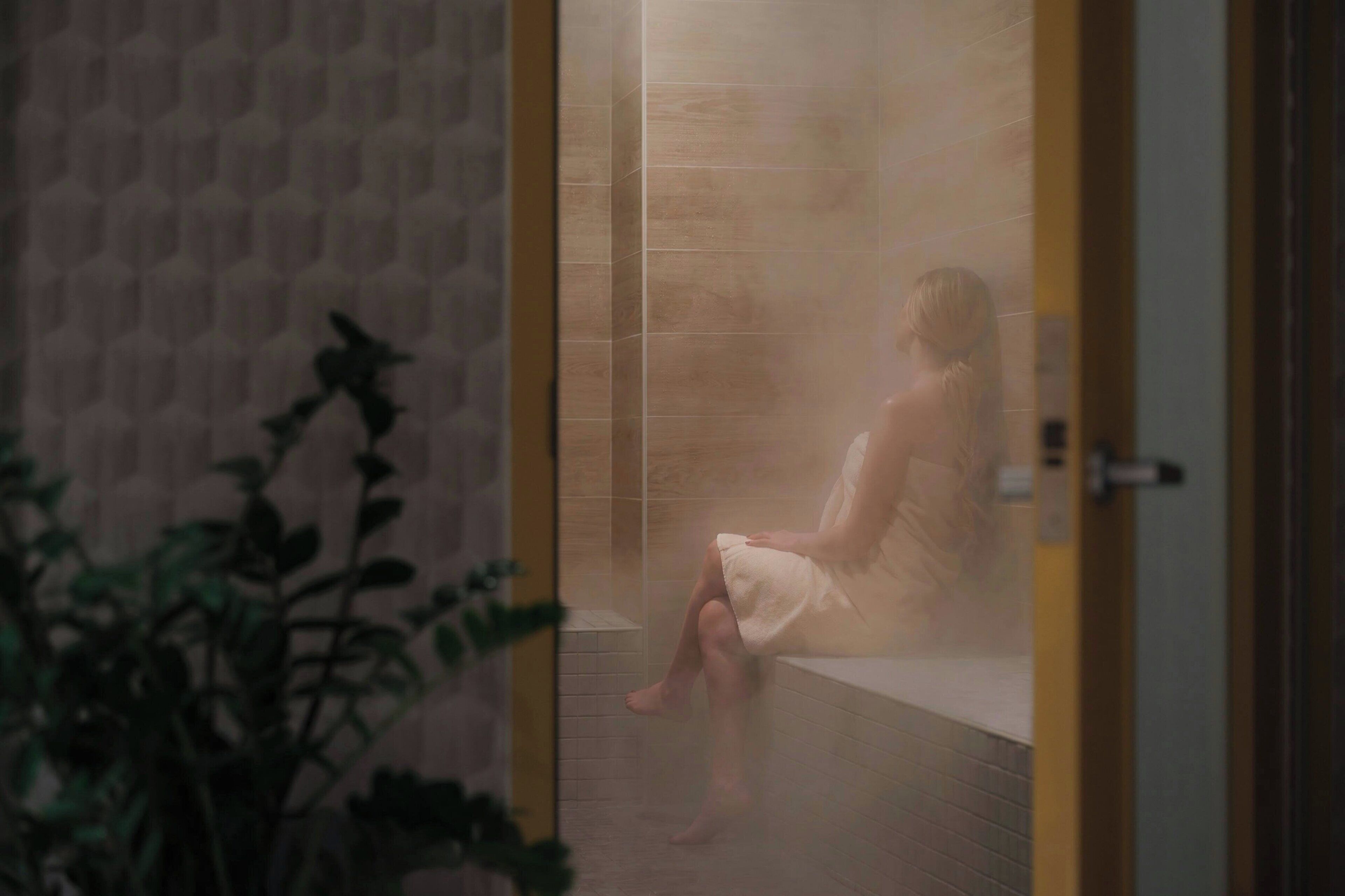 Une personne assise dans un hammam aux murs carrelés et à la porte en bois.