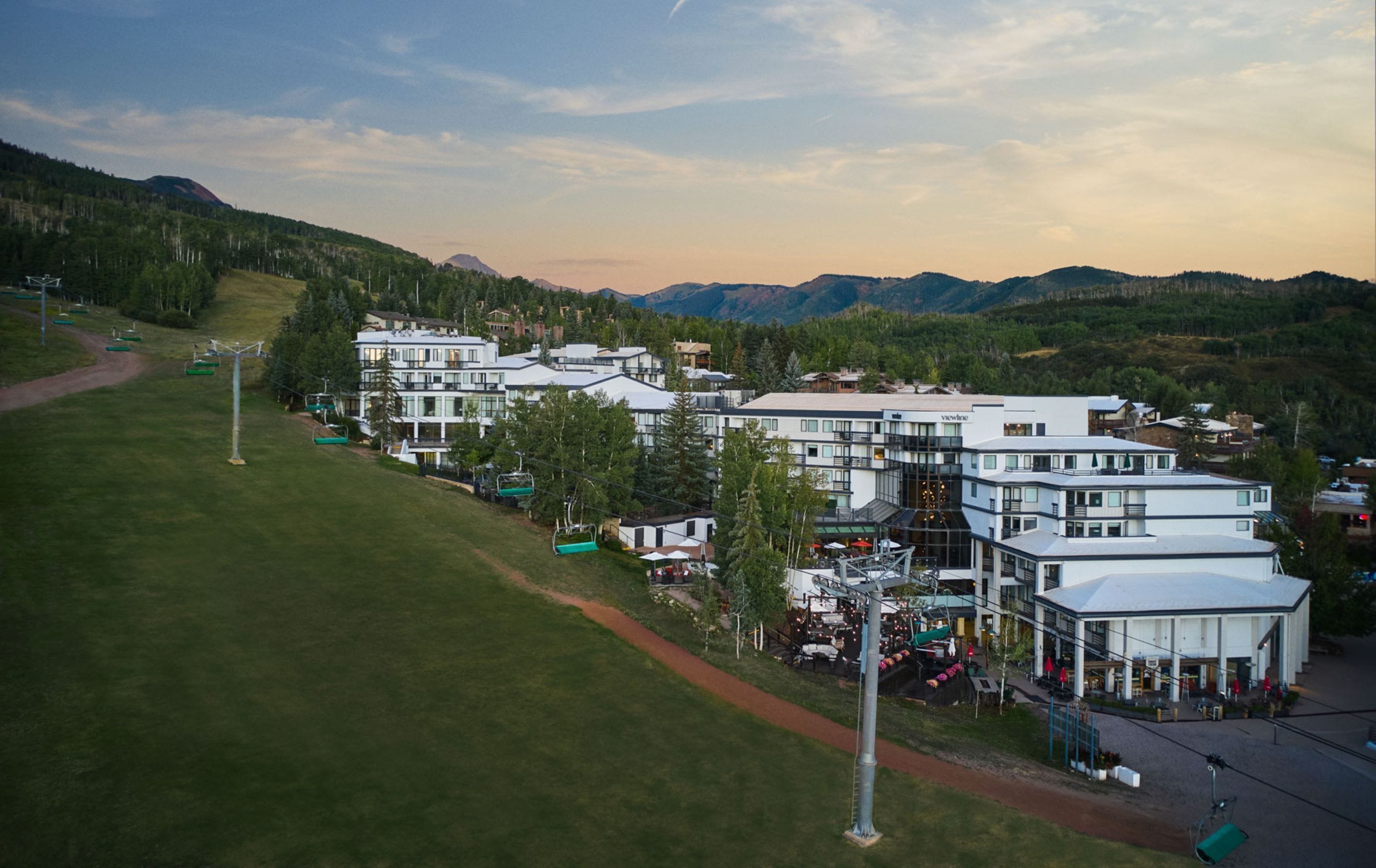 A modern hotel complex with multiple buildings, a ski lift, and a mountainous backdrop.
