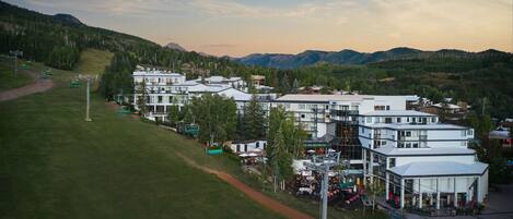 A modern hotel complex with multiple buildings, a ski lift, and a mountainous backdrop.