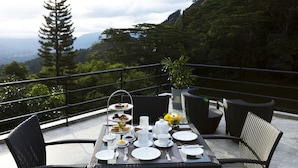 A table set for a meal with plates, cups, and a tiered dessert stand, overlooking a mountainous landscape. - Hunas Falls Hotel (Ukuwela)