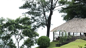 A thatched-roof structure on a grassy hill with trees in the background. - Hunas Falls Hotel (Ukuwela)
