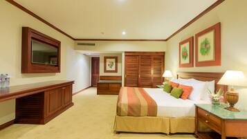 A hotel bedroom with a large bed, a wooden wardrobe, a desk, a mirror, and a television.