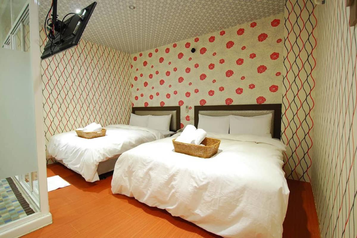 A hotel room with two beds, each with white linens and a basket of towels. The walls have a patterned wallpaper with red flowers.