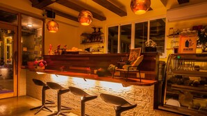 Una zona de bar con pared de piedra, mostrador de madera y tres taburetes negros.