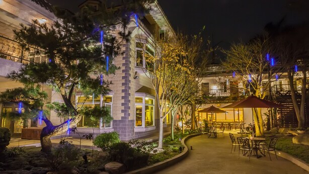 Un hotel con fachada de piedra, mesas al aire libre y árboles iluminados.
