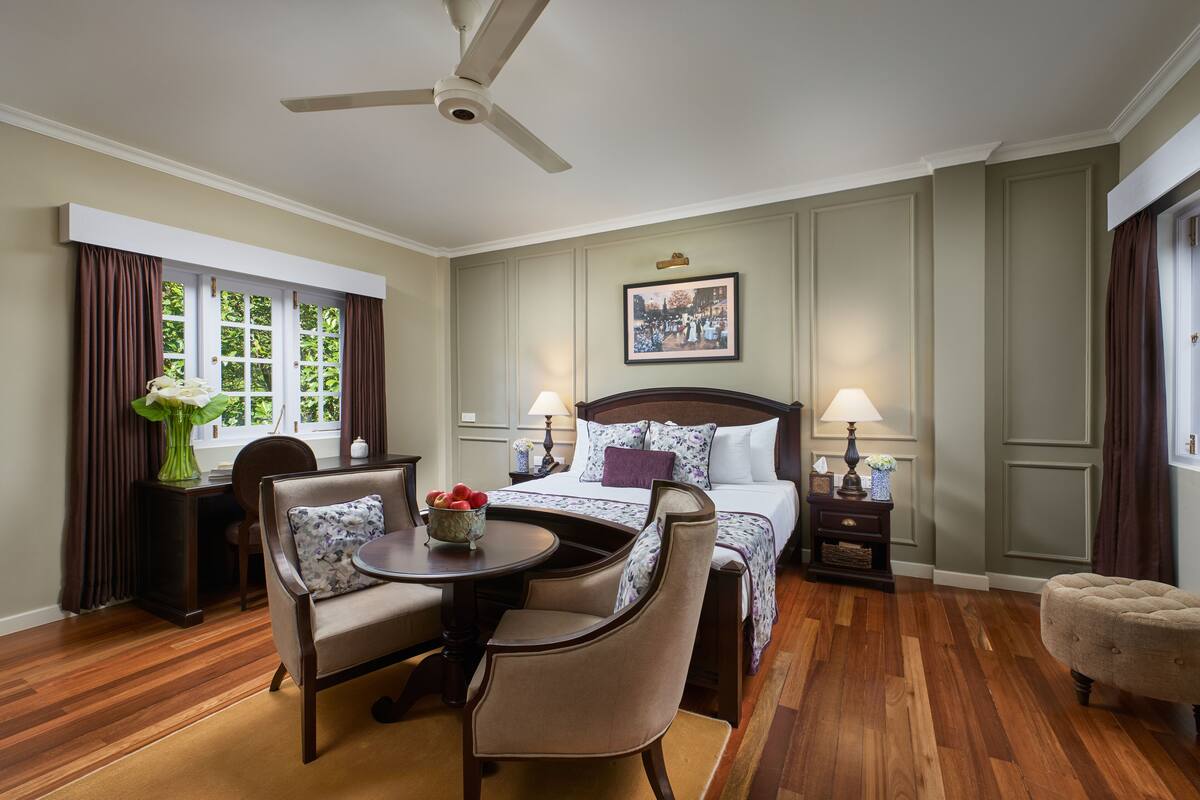 Ein Hotelzimmer mit Bett, Schreibtisch, Stuhl, rundem Tisch und Deckenventilator.