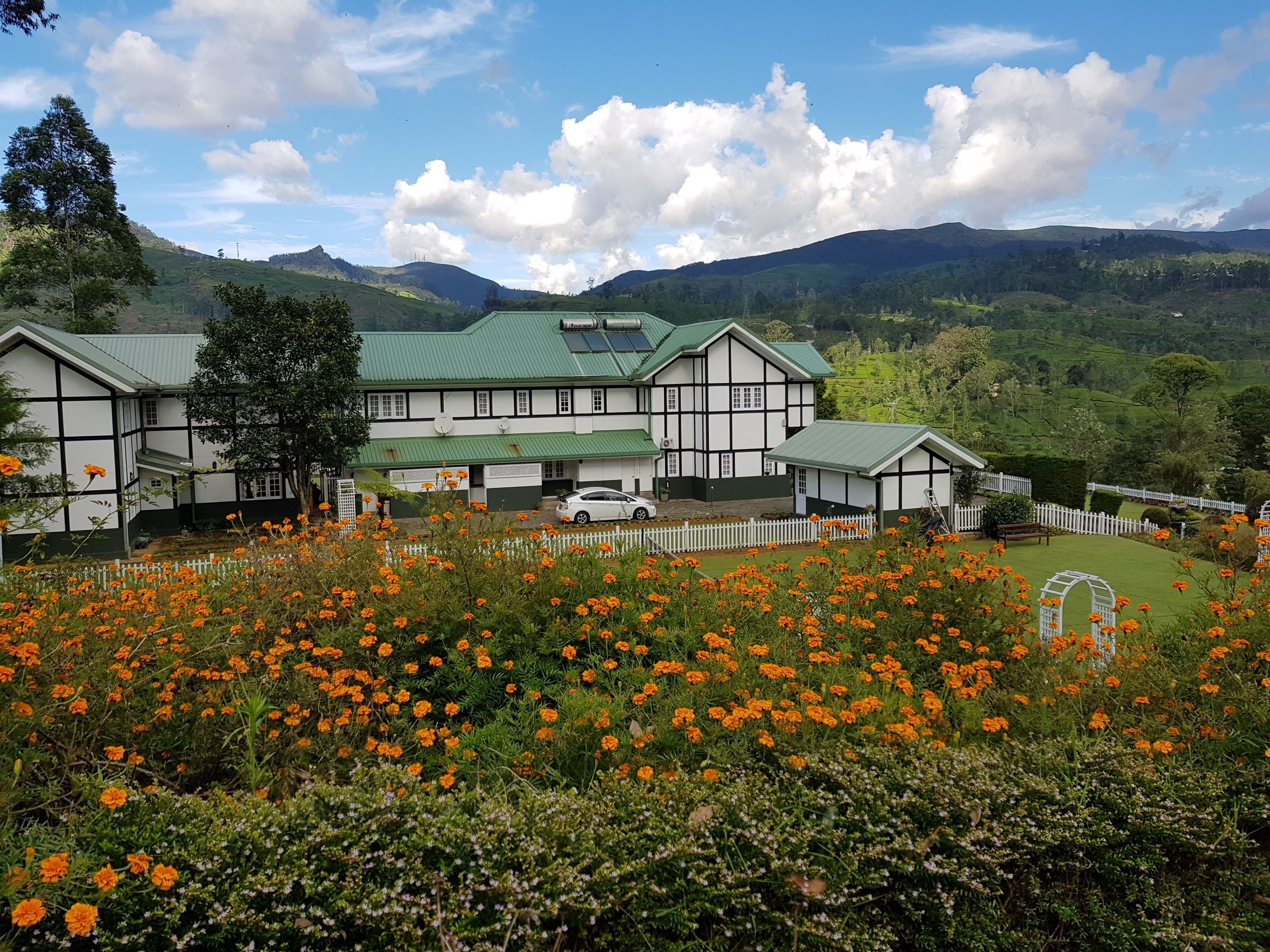 A traditional building with a green roof, surrounded by a white picket fence and vibrant orange flowers.